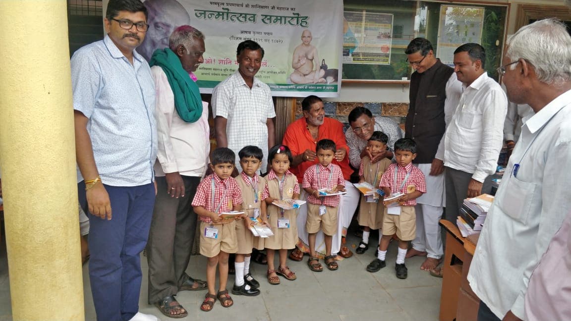 Schoolchildren in uniform holding their new books, with teachers and Foundation members, in front of a school banner.