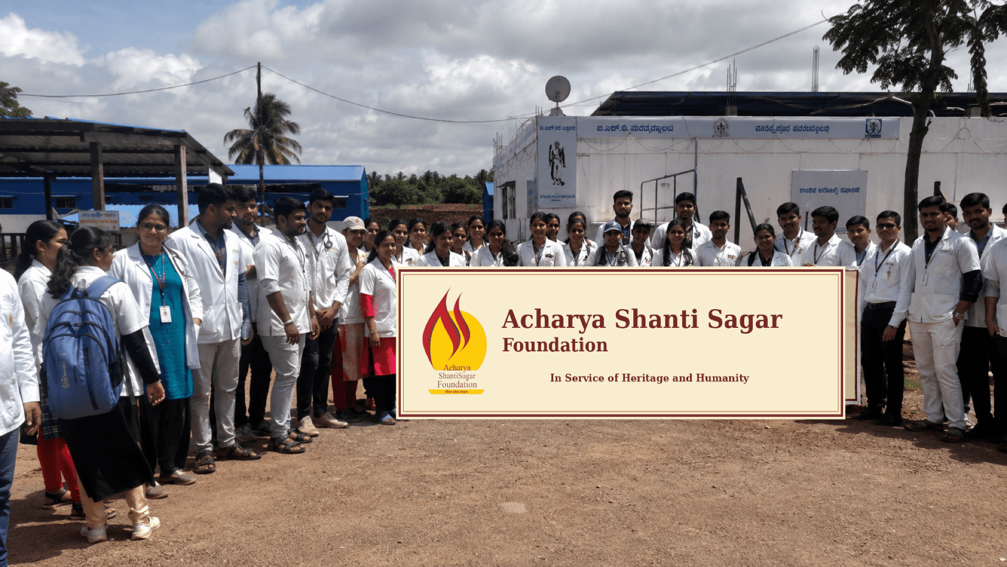 Doctors, nurses and volunteers standing in rows behind an Acharya Shanti Sagar Foundation banner at a free health camp.