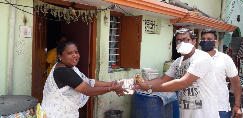 Masked volunteers handing a food packet to a woman at her doorway.