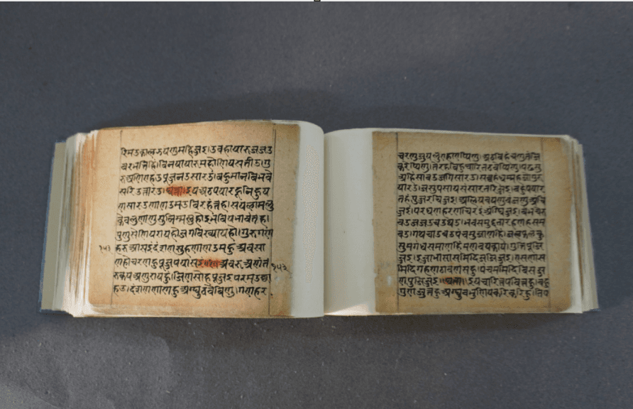 An opened volume of handwritten Devanagari paper folios, with ruled margins, red highlighting and folio numbers in the margin.
