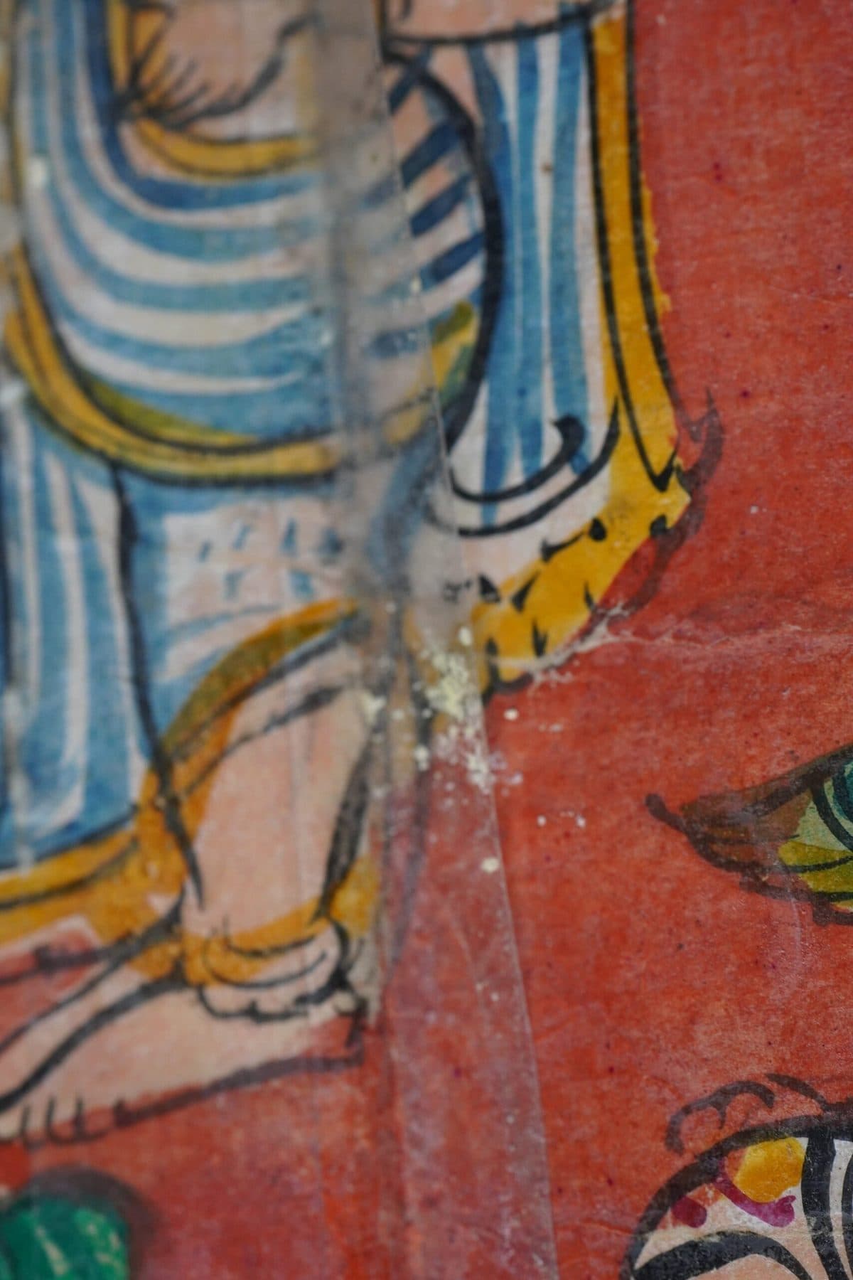 Close view of painted cloth, the paint cracked and lifting along a fold.