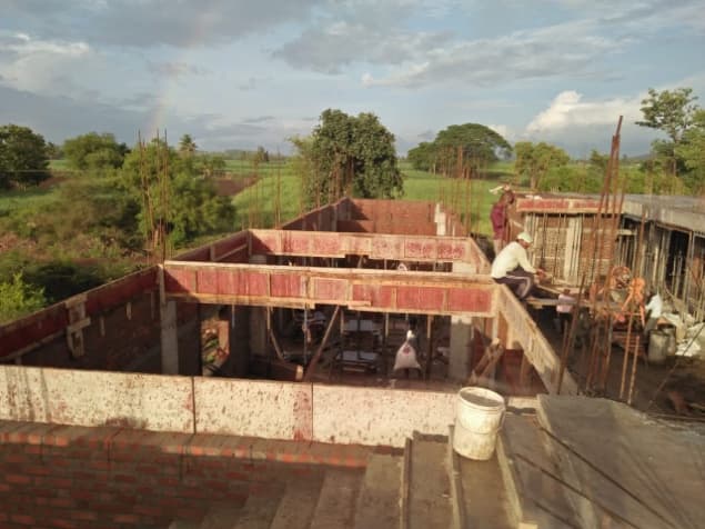 Brick walls and red shuttering of the hall under construction, a worker on the wall.